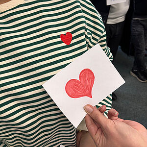 Ein gemaltes Herz auf Papier vor einem Pullover mit Herz
